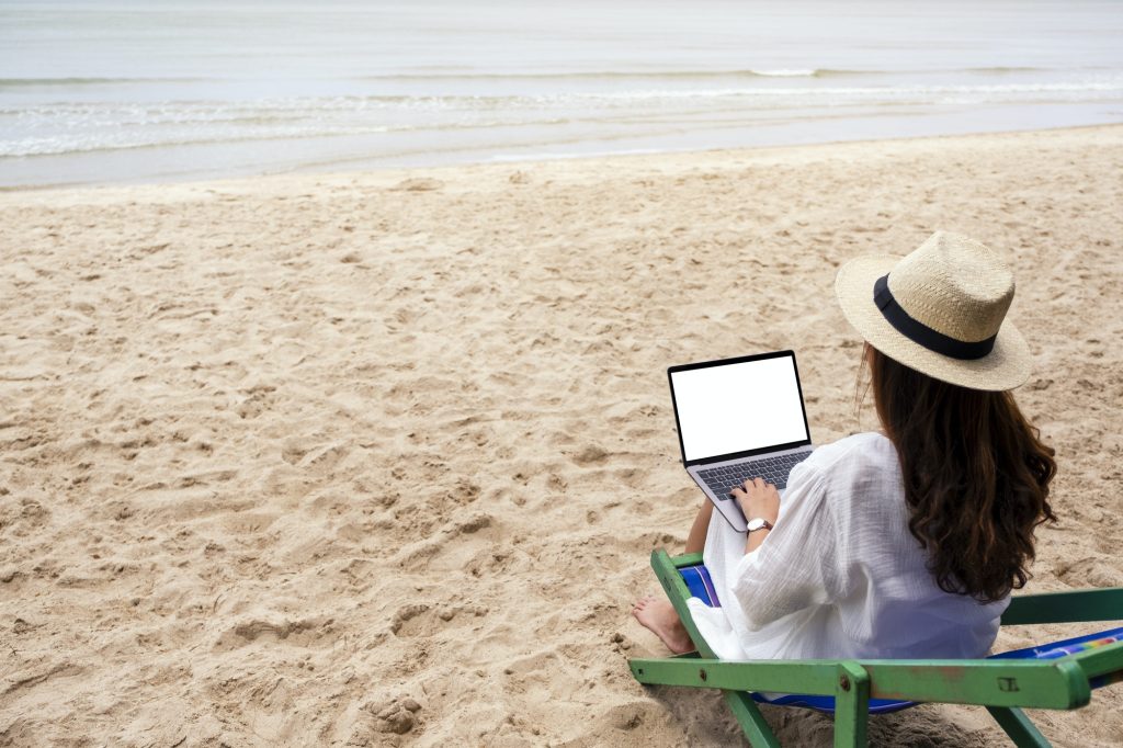 A woman using and typing on laptop computer with blank desktop screen on a beach chair